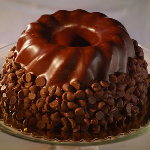 Chocolate bundt cake with glossy glaze and chocolate chips on bottom half, displayed on a glass stand.