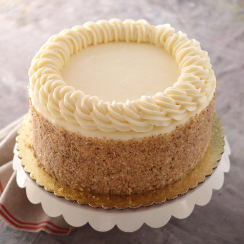 Round cake with white frosting, rosettes, nut-covered sides, on a white stand with gold cake board.