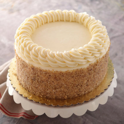 Round cake with white frosting, rosettes, nut-covered sides, on a white stand with gold cake board.