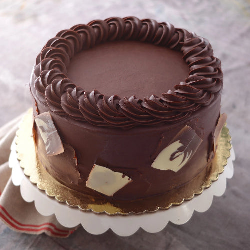 Round cake with dark chocolate frosting, thick piped border, dark and white chocolate shards, on gold board.